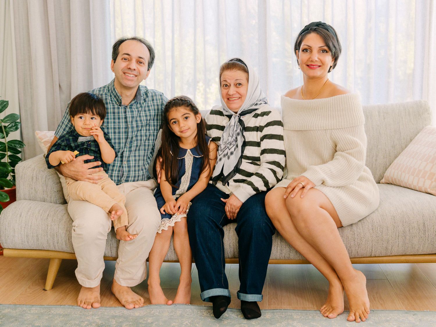A happy family of five poses together on a gray sofa in a bright, modern living room.