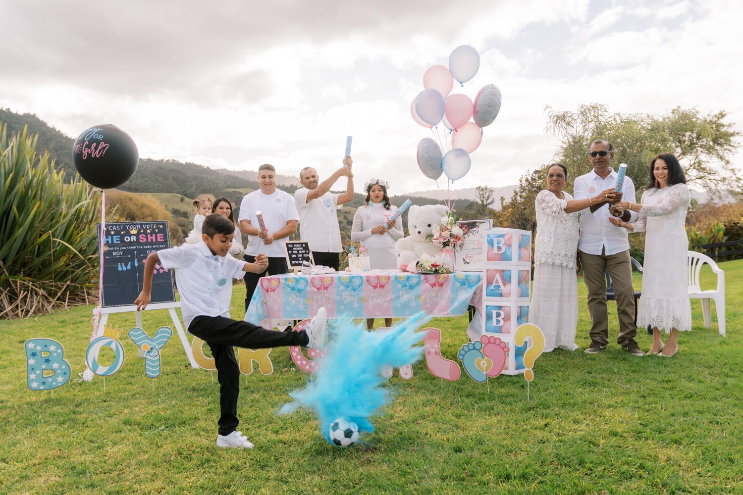 A joyful gender reveal party outdoors with blue powder burst, balloons, and excited guests celebrating a baby boy announcement.
