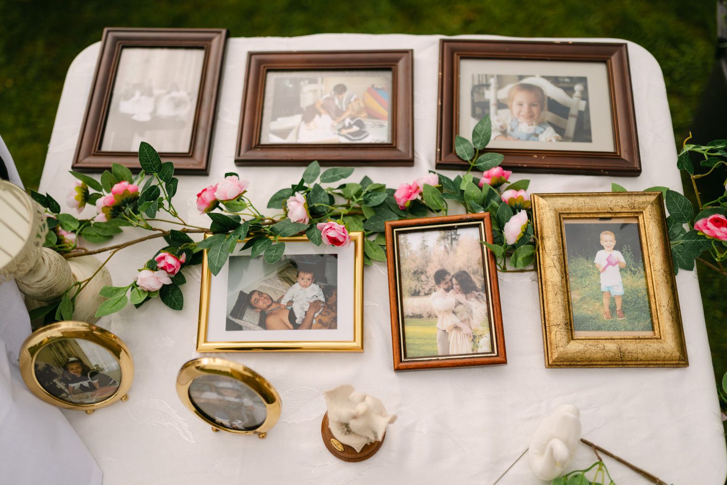 A decorative wedding memory table with framed family photos, pink roses, and gold frames arranged on a white linen cloth.