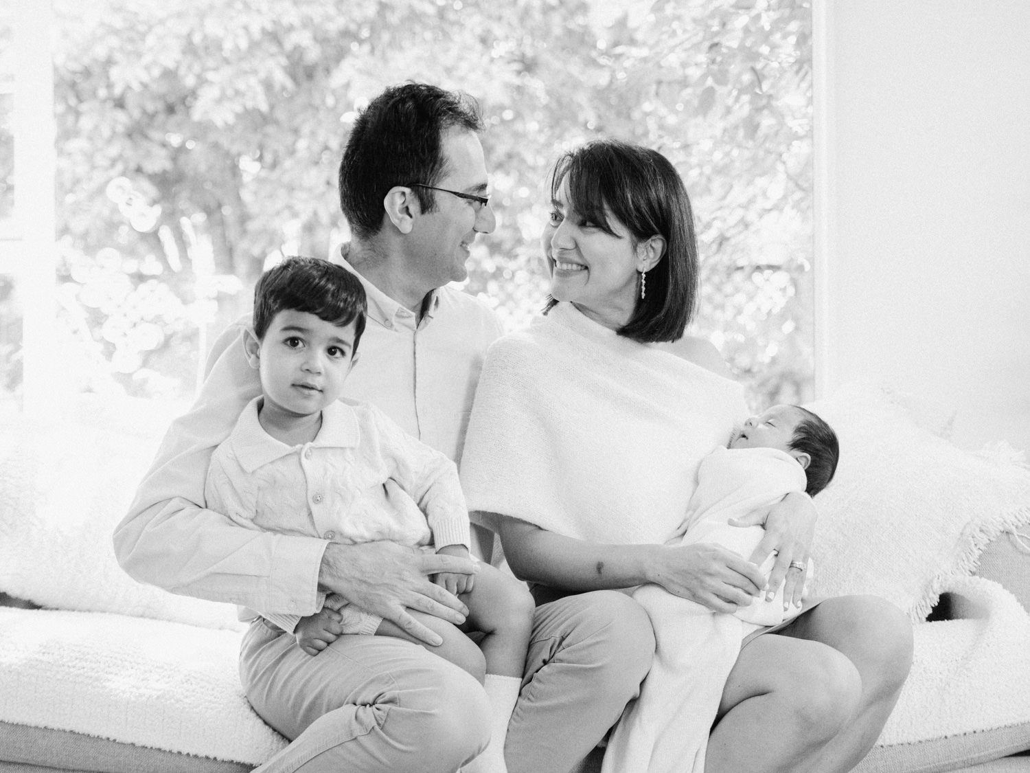 Black and white family portrait with parents and two children including newborn baby on sofa.