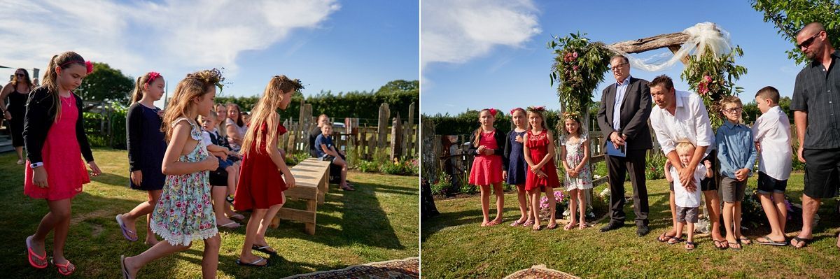 Outdoor wedding ceremony with guests gathered on a sunny lawn, children and adults celebrating near a floral arch.