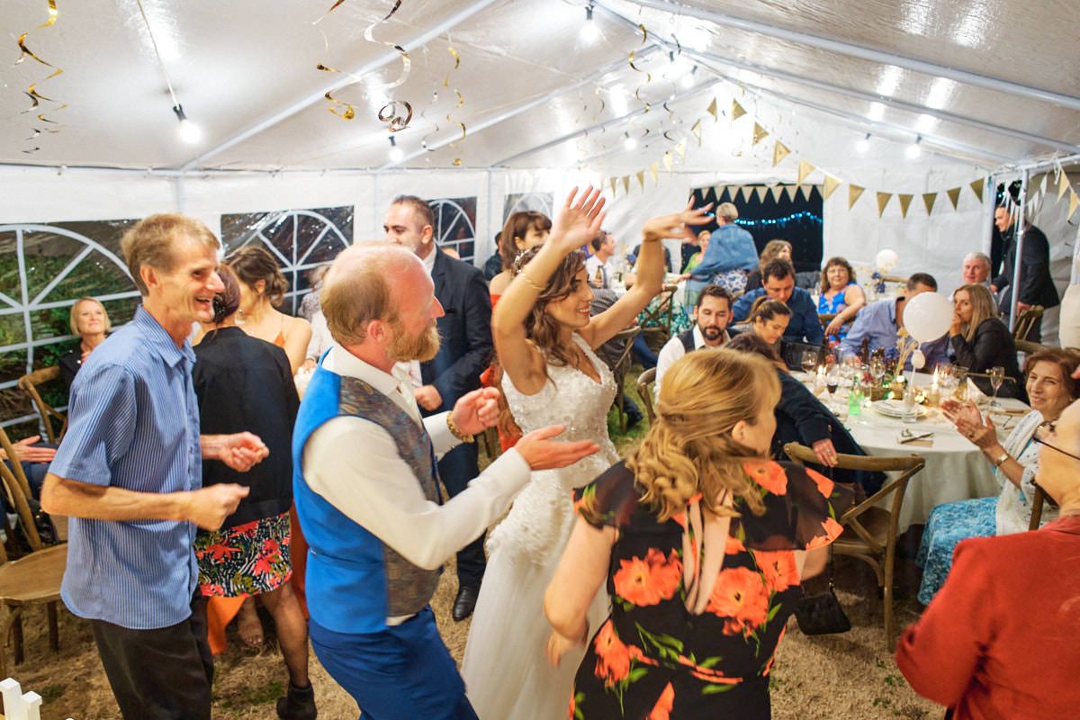 Wedding reception dance floor with bride and groom celebrating with guests under a decorated marquee tent.