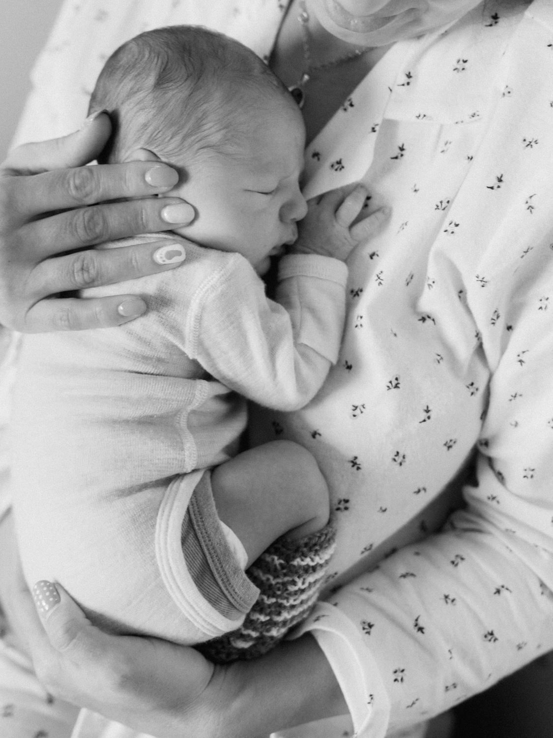 Close-up black and white image of a sleeping newborn baby cradled in a mothers arms wearing knit booties.