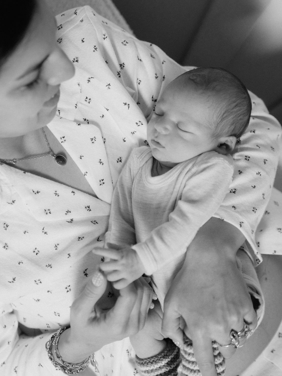 Black and white photo of a mother cradling her sleeping newborn baby, wearing a floral dress and bracelets.