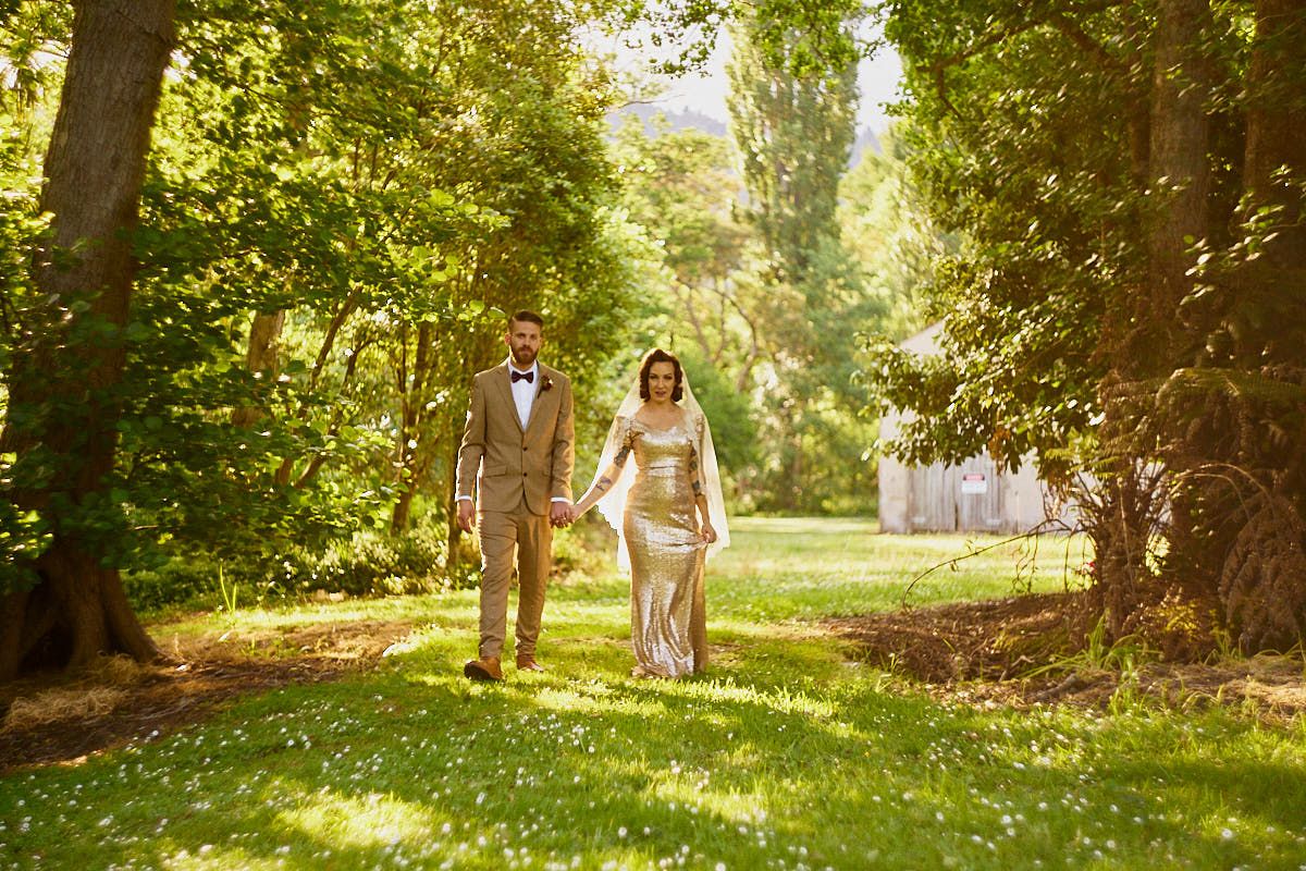 Bride and groom walking hand in hand through a lush green tree-lined path on their wedding day.