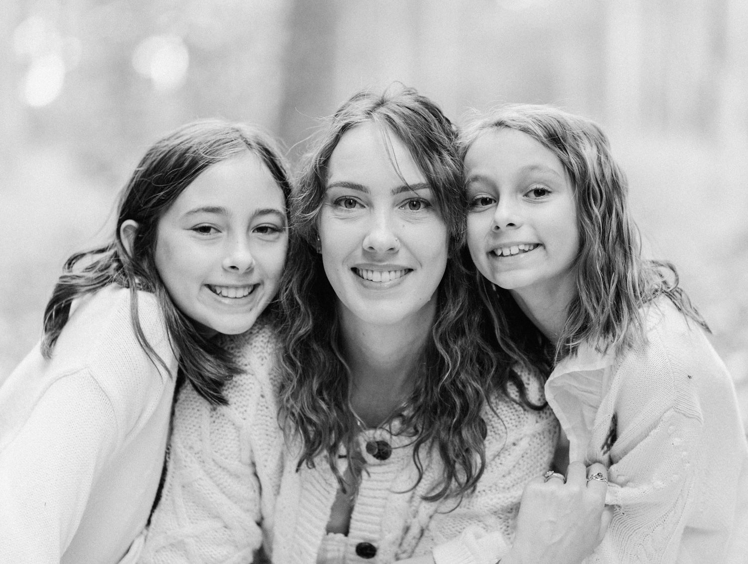 Black and white portrait of three smiling girls posing together outdoors in a candid, joyful photo.