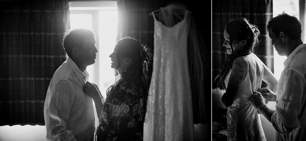 Black and white wedding photo of bride and groom sharing an intimate moment with wedding dress hanging in background.