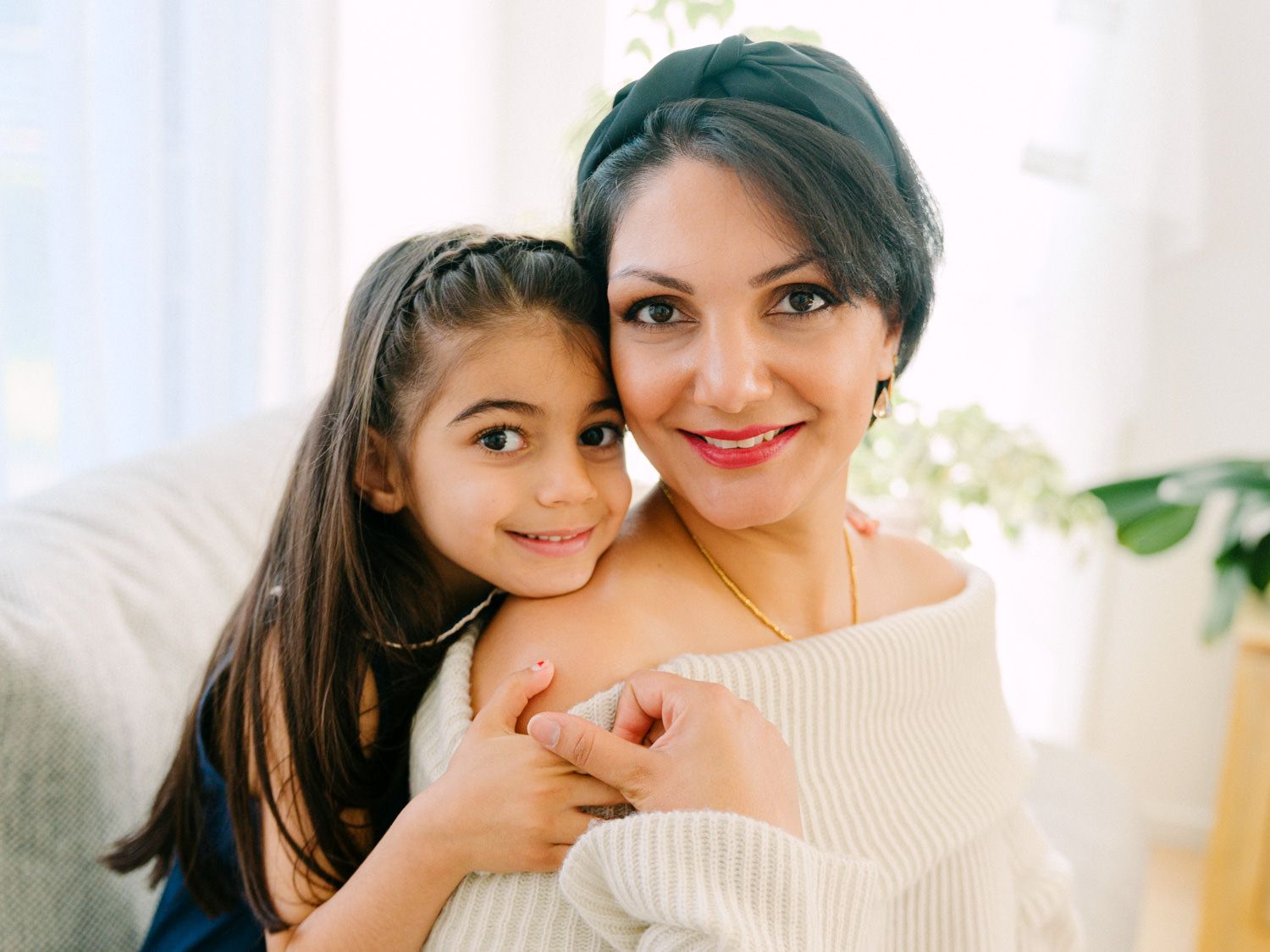 A woman and young girl smiling together in a bright, cozy indoor setting, sharing a warm embrace.
