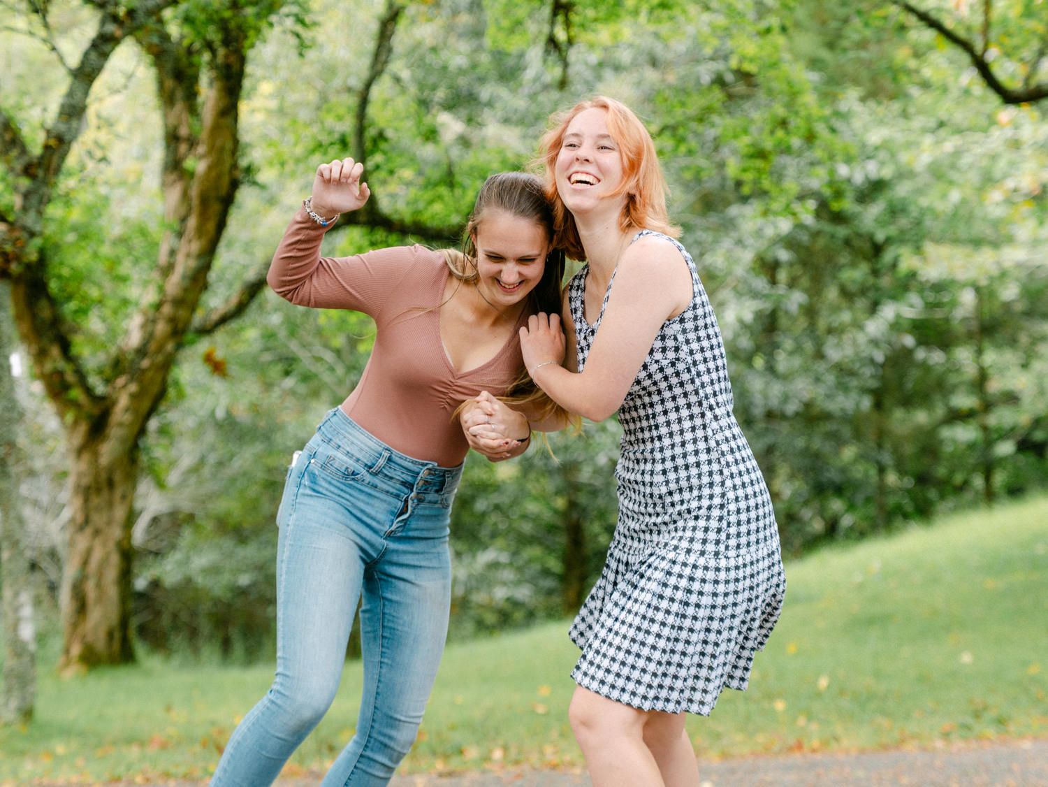 Two young women laughing and playfully posing together outdoors in a lush green park setting.