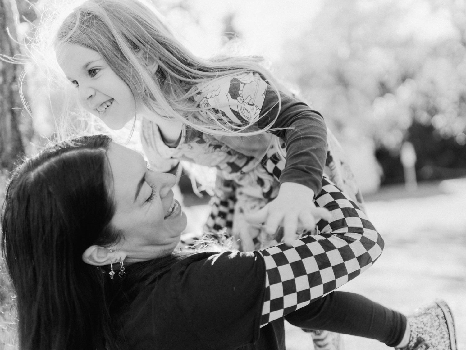 Black and white photo of a woman joyfully lifting a laughing young girl in a park.