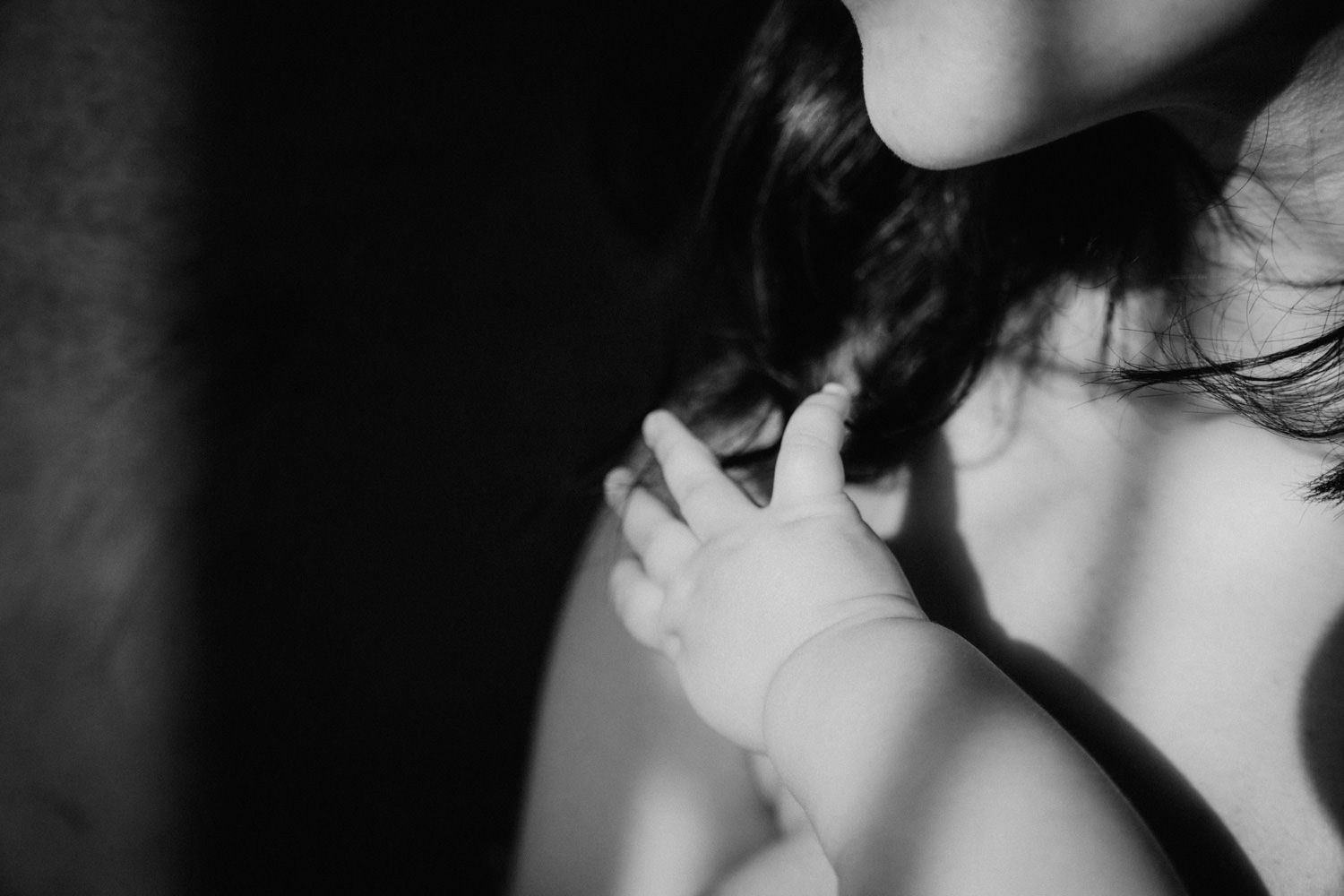 Black and white photo of a mother holding her newborn baby's tiny hand against her shoulder.
