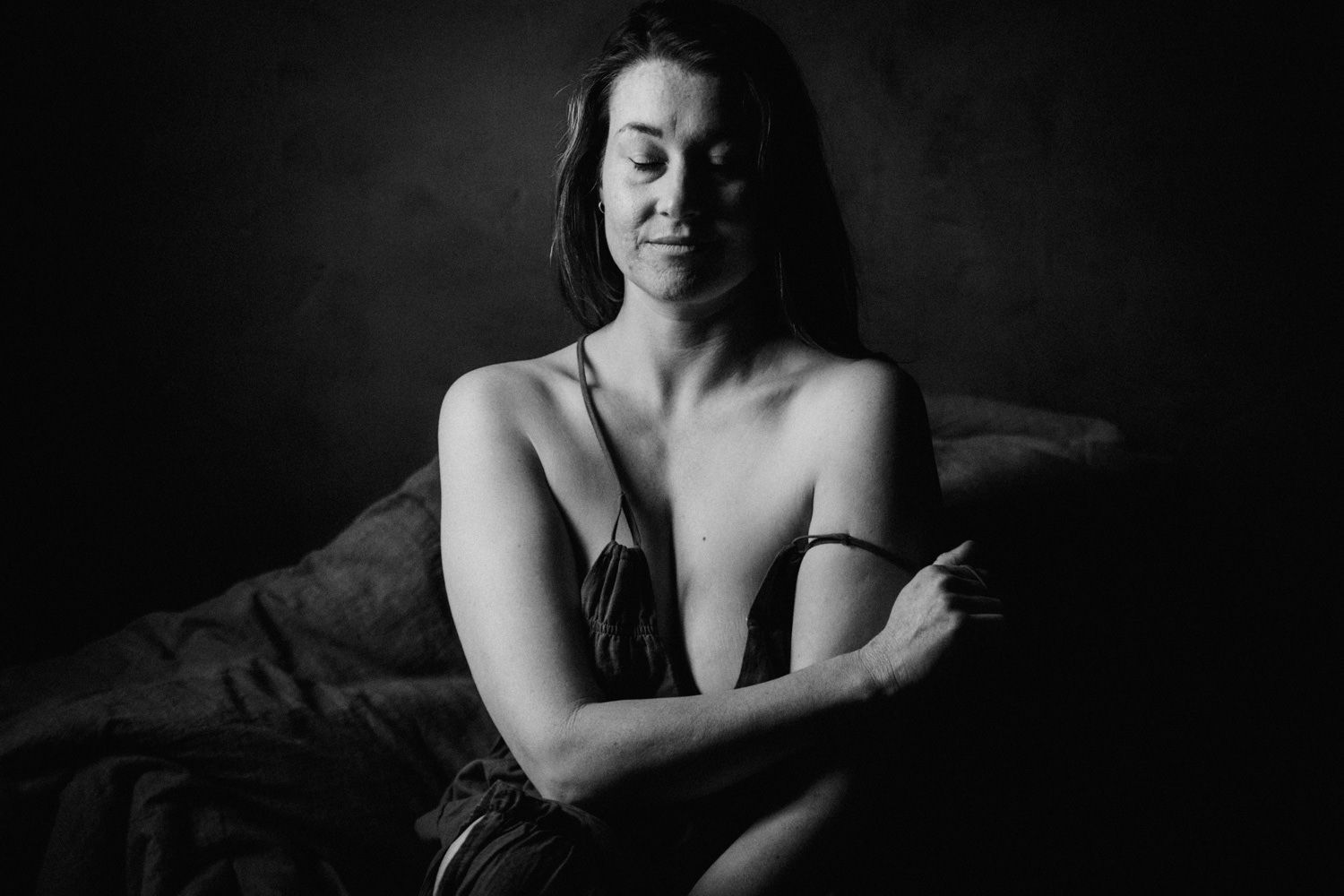 Black and white fine art portrait of a woman seated against dark background in dramatic lighting.