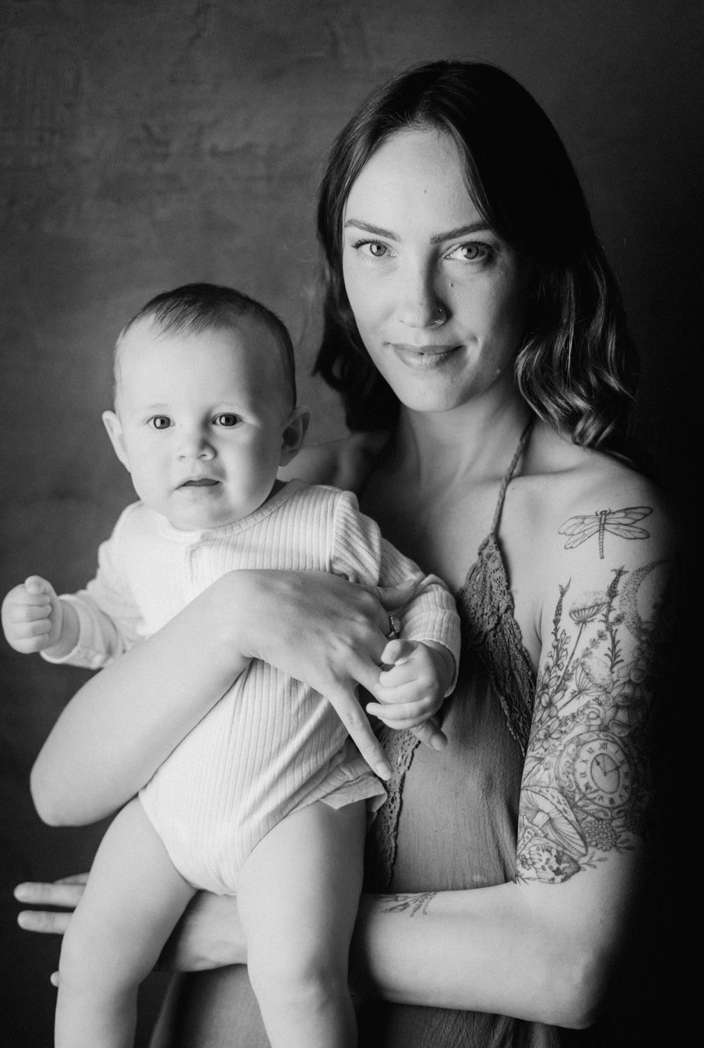 Black and white portrait of a tattooed mother holding her baby, studio photography.
