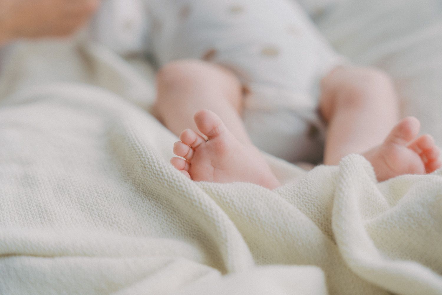 Close-up of newborn baby feet resting on a soft white knit blanket.