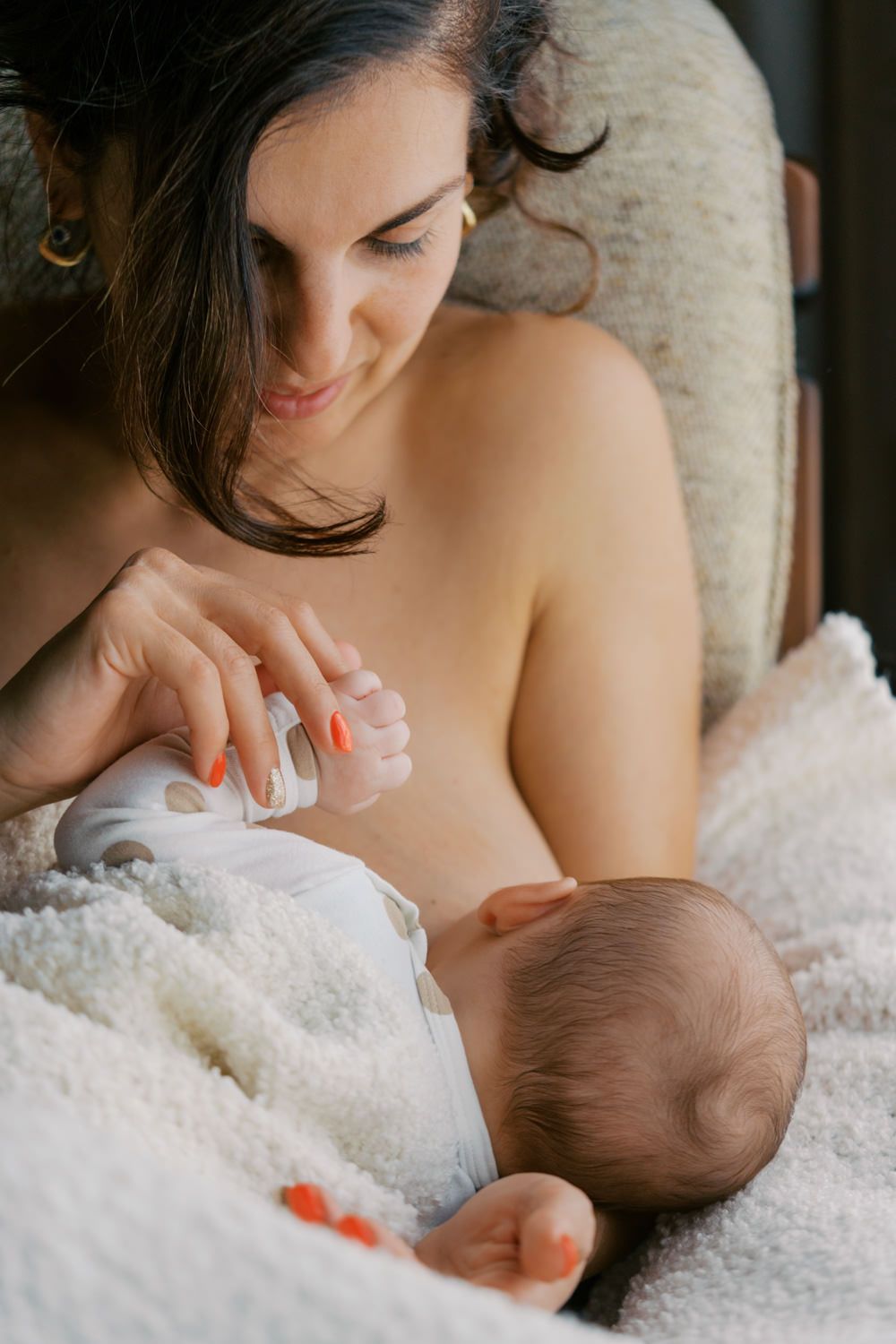 A mother lovingly bottle-feeds her newborn baby while seated in a cozy chair.