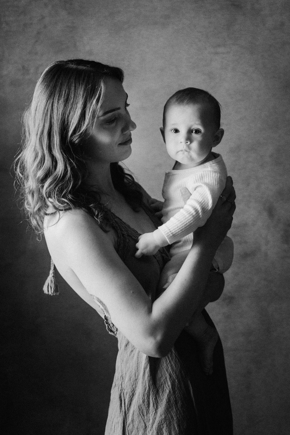 Black and white portrait of a young mother tenderly holding her baby in a studio setting.