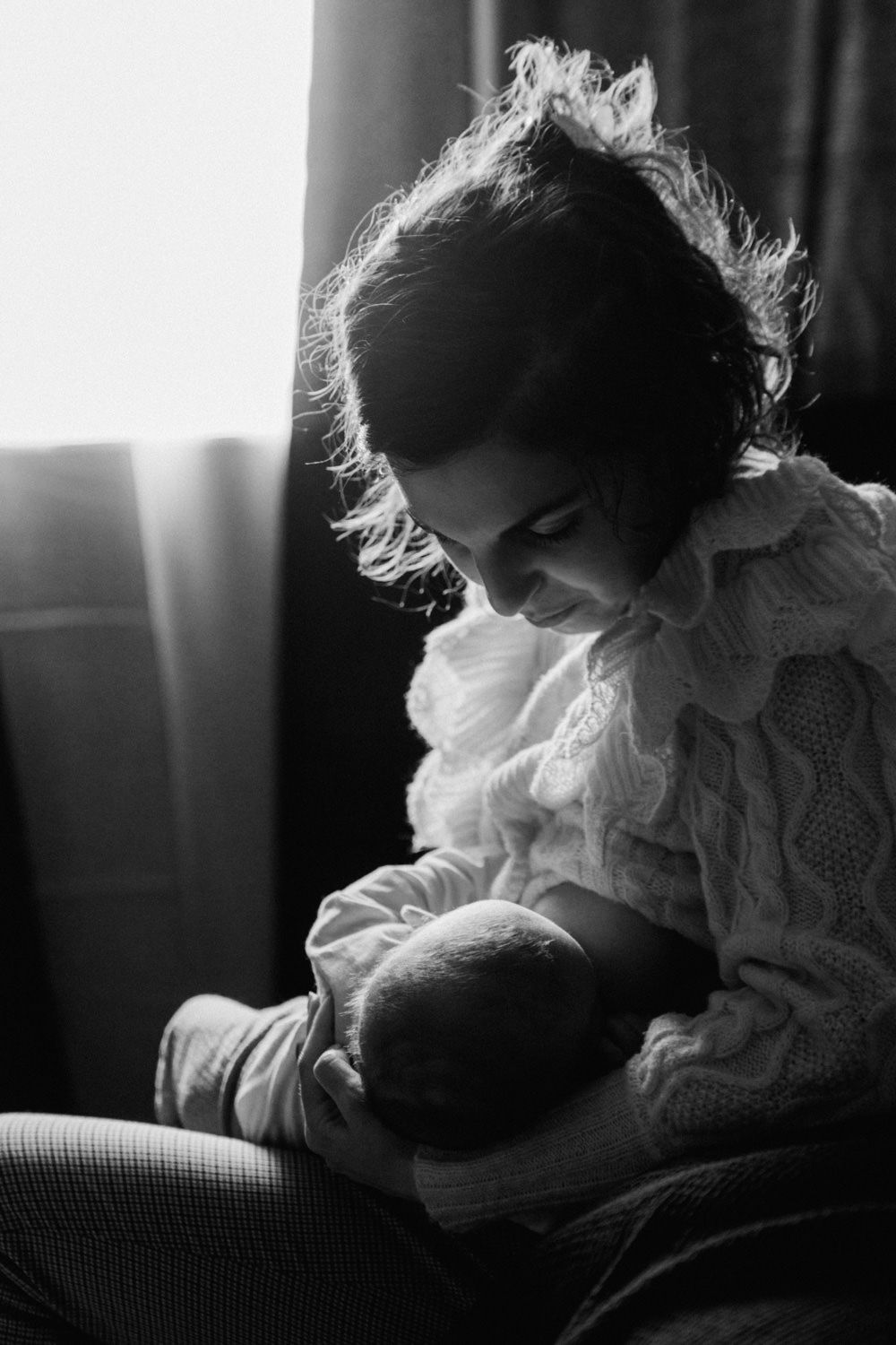 Black and white photo of a mother tenderly breastfeeding her newborn baby by a window.