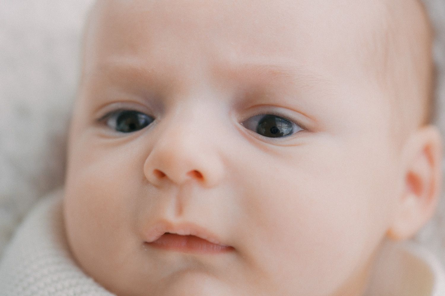 Close-up portrait of a newborn baby with blue eyes and soft skin, looking curiously at the camera.