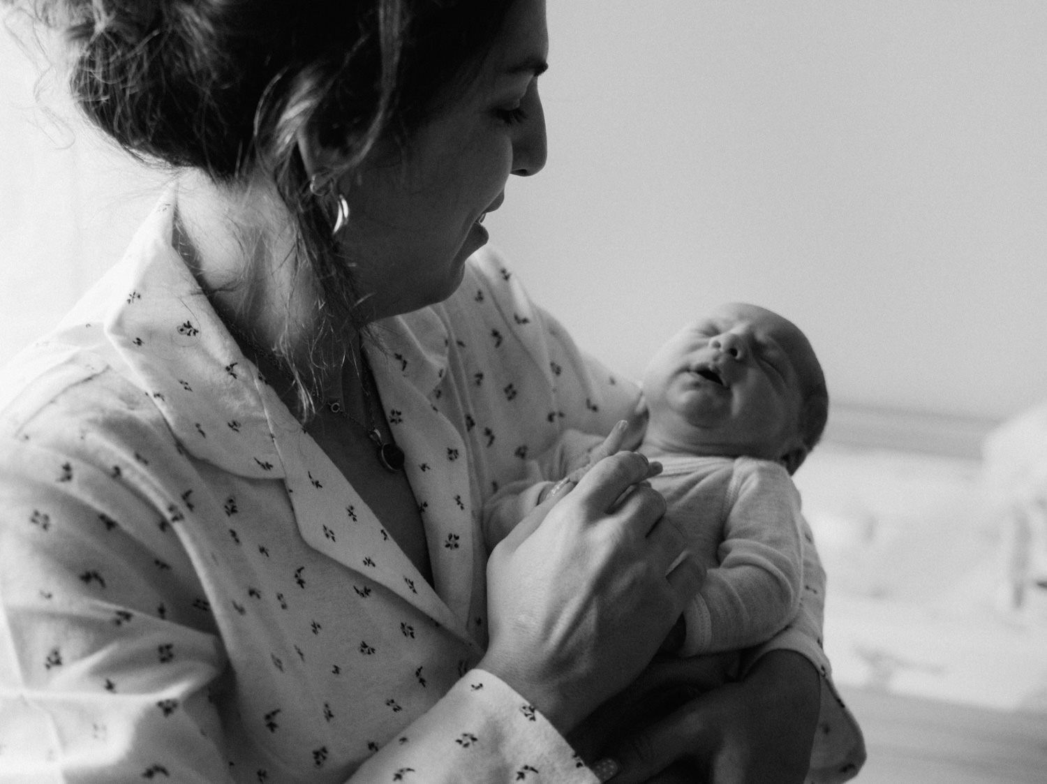 Black and white photo of a new mother in hospital gown tenderly holding her newborn baby.