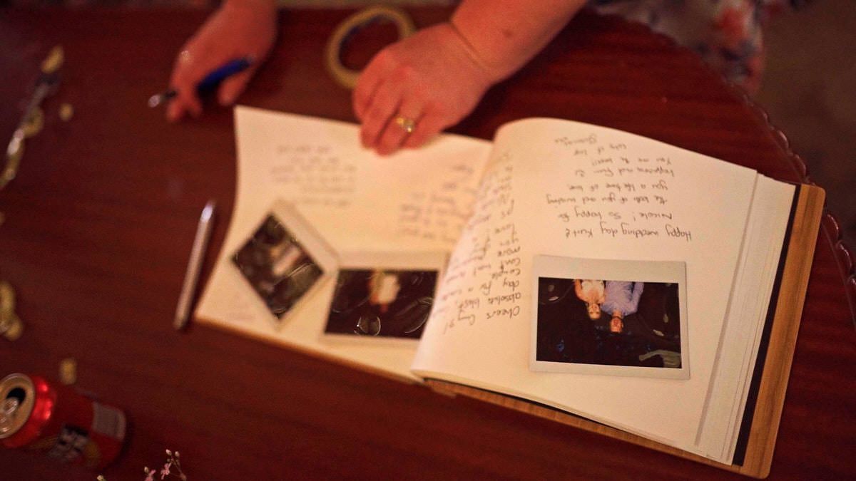 A baby's hand rests on an open scrapbook with handwritten notes and ultrasound photos on a wooden table.