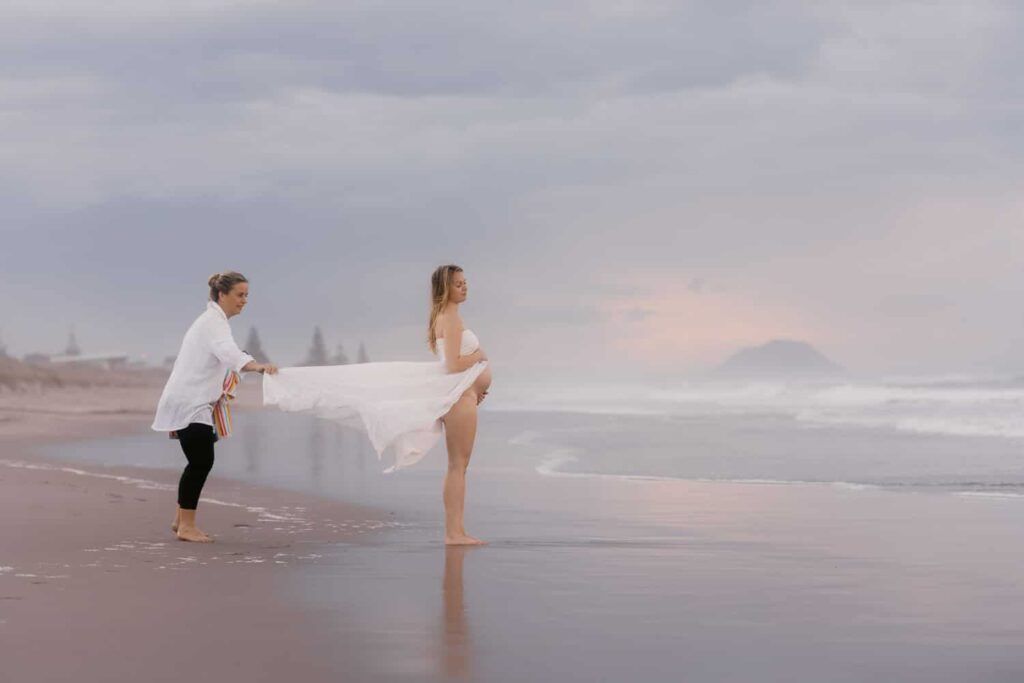 Couple sharing a romantic moment on a serene beach at dusk, woman in white bikini holding flowing fabric.