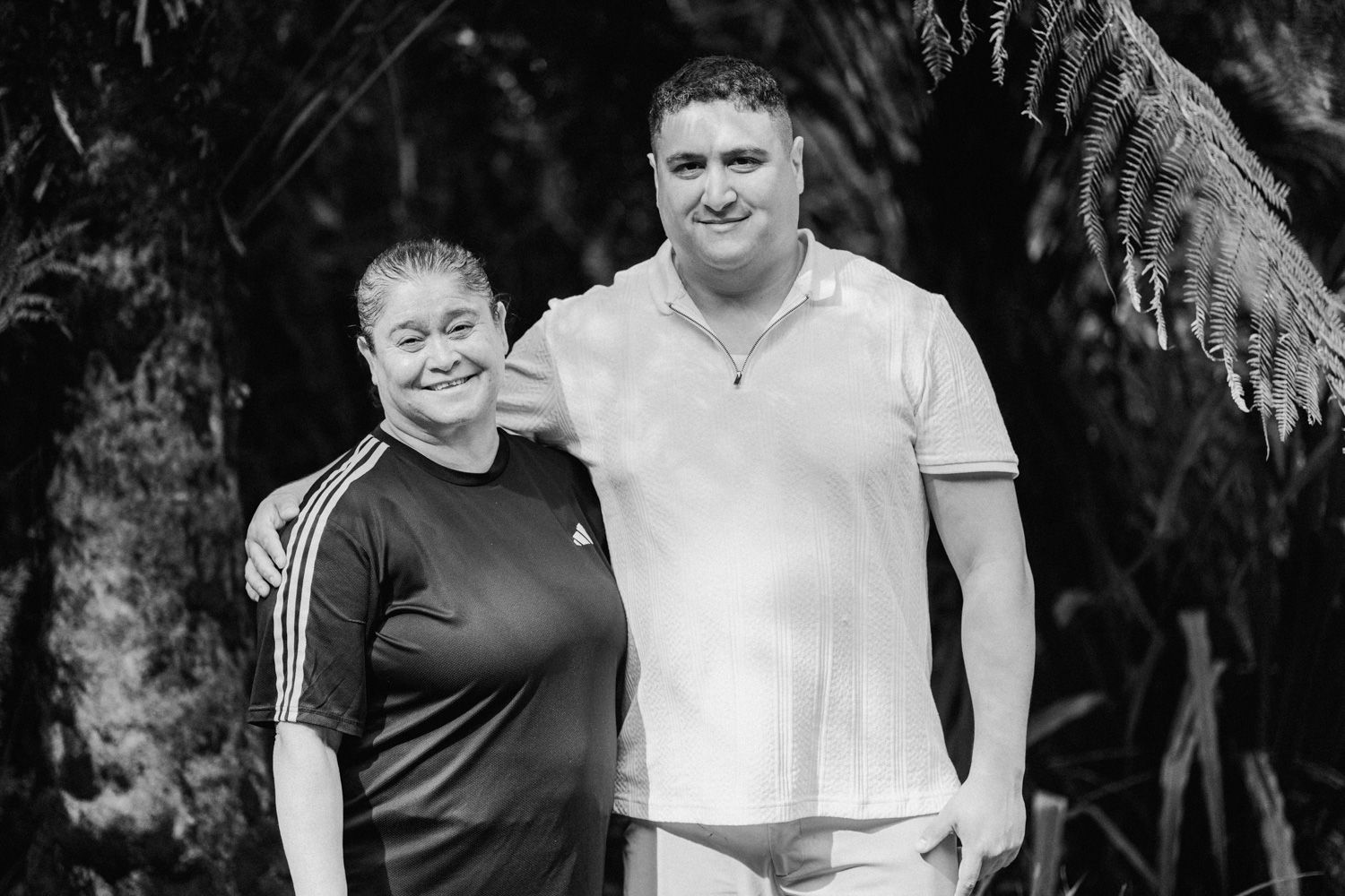 Black and white photo of a smiling man and woman posing together outdoors among tropical palm trees.