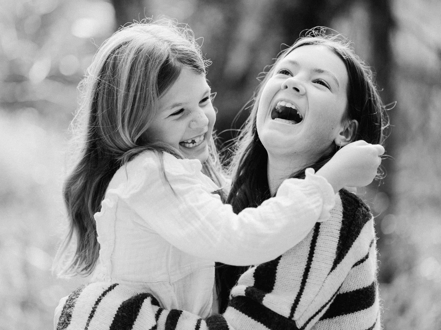 Black and white photo of a mother and young daughter laughing joyfully together outdoors in a candid moment.