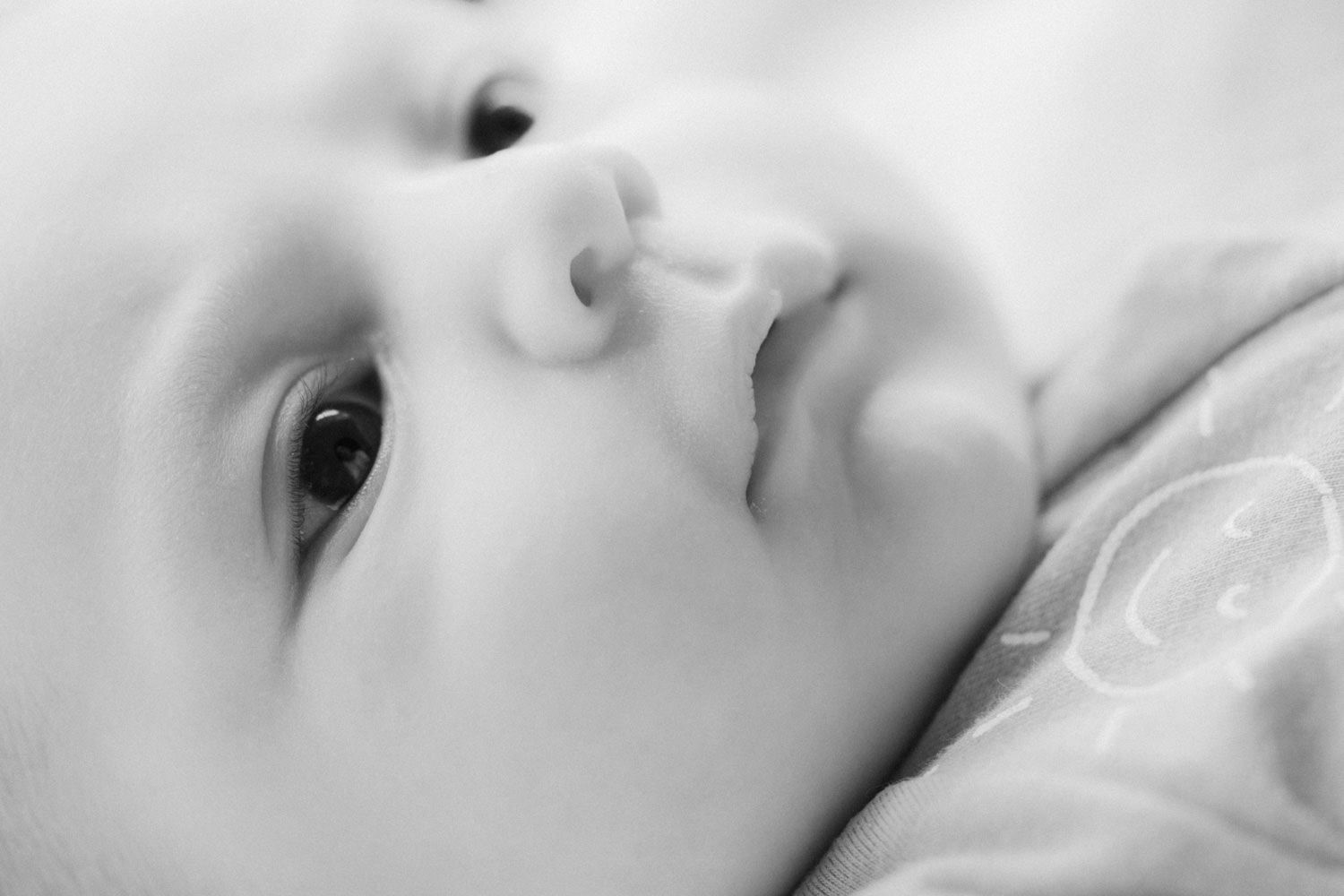 Close-up black and white portrait of a peaceful newborn baby gazing upward with soft, delicate features.