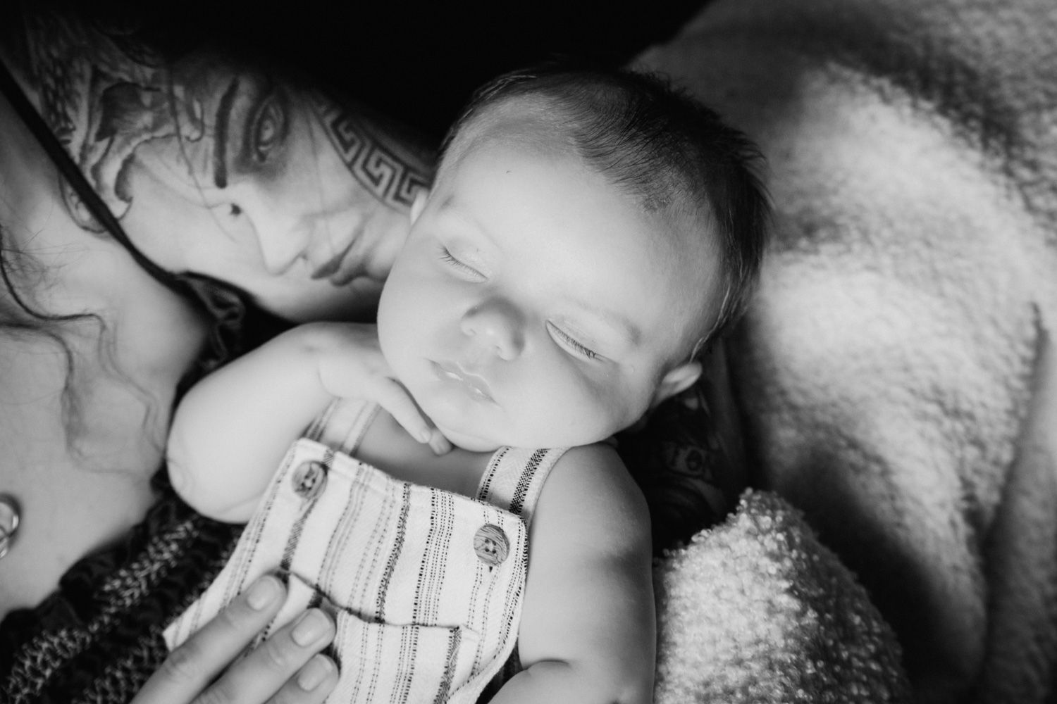 Black and white photo of a sleeping newborn baby in striped overalls cuddled close to mother.
