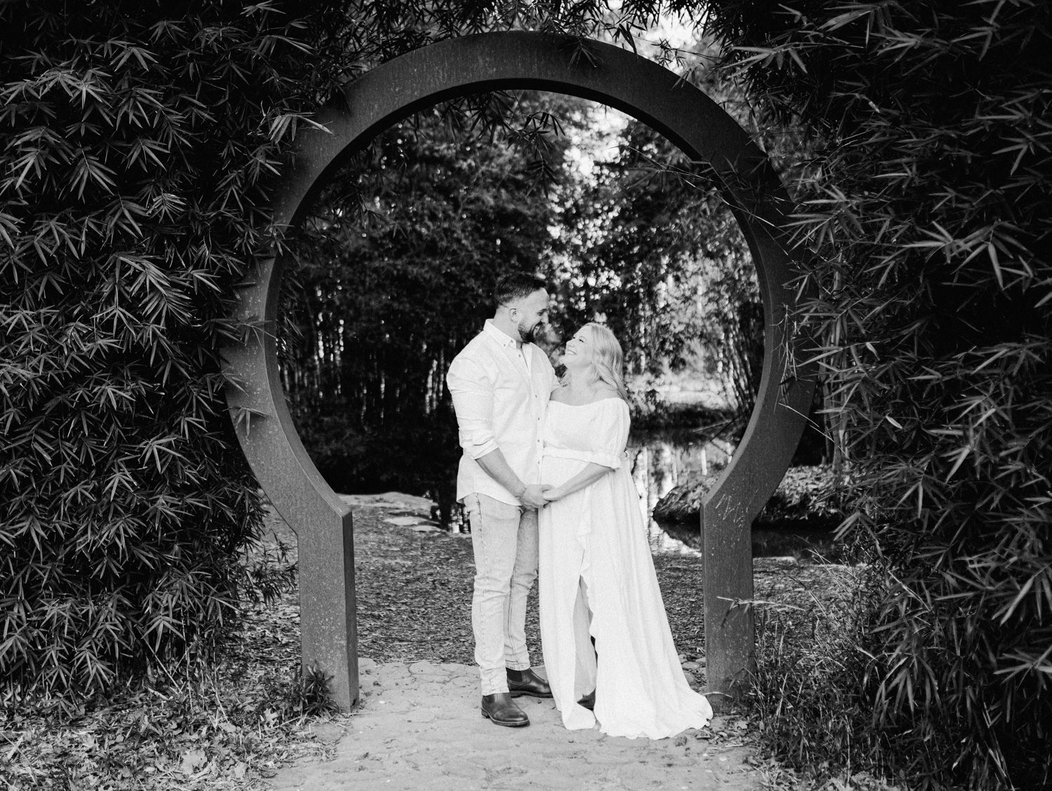 Black and white photo of a couple kissing under a circular arch surrounded by lush bamboo in a garden.