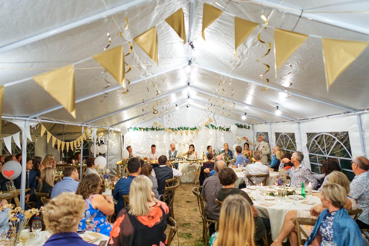 Guests celebrate under a decorated tent with bunting and string lights at an elegant outdoor party or wedding reception.