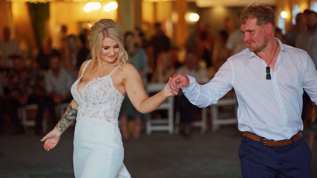 Bride in white lace gown and groom in blue shirt dance joyfully at their elegant wedding reception.
