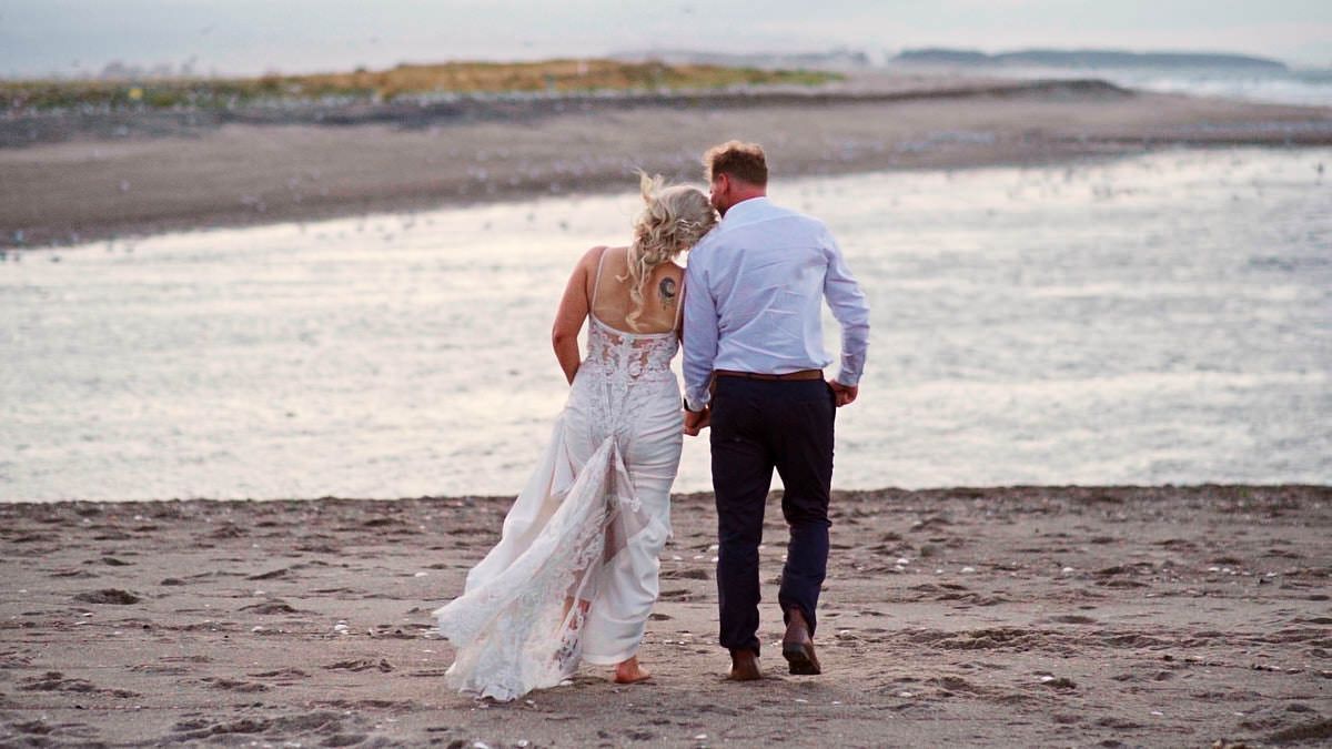 Bride and groom walking hand in hand on a sandy beach at sunset in wedding attire.