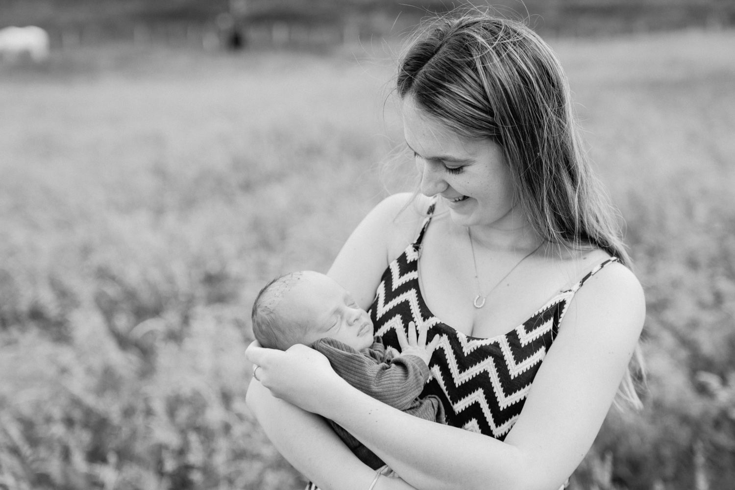 Black and white photo of a young mother cradling her newborn baby in an outdoor field setting.