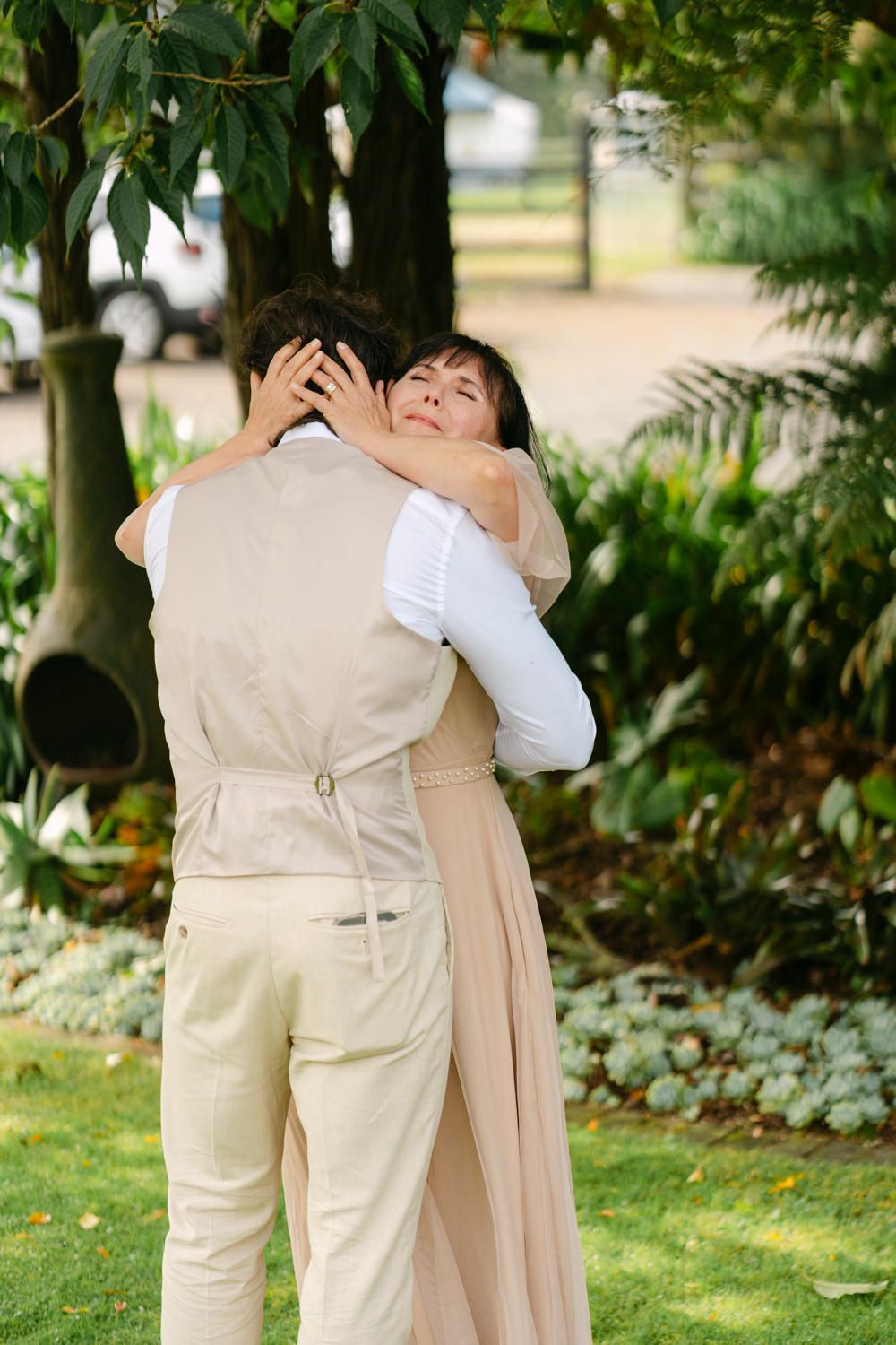 Couple sharing a tender embrace in a lush garden, wearing elegant beige wedding attire.