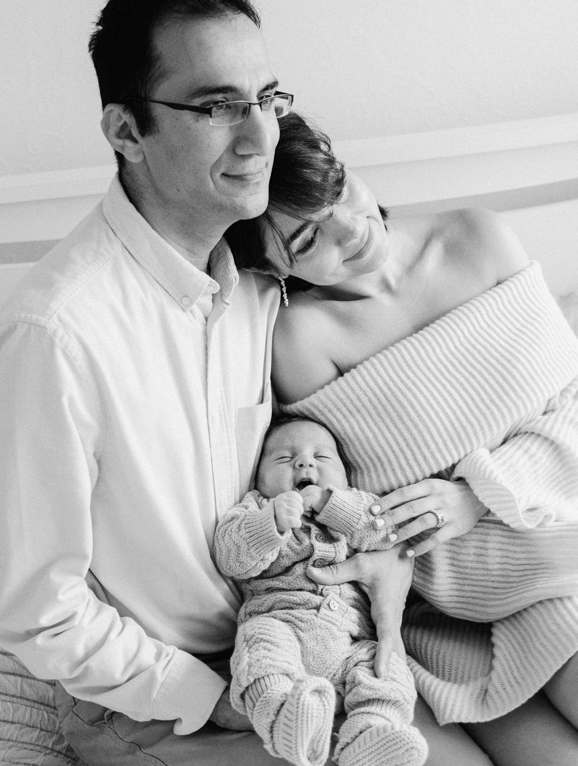 Black and white photo of happy parents holding their smiling newborn baby together.