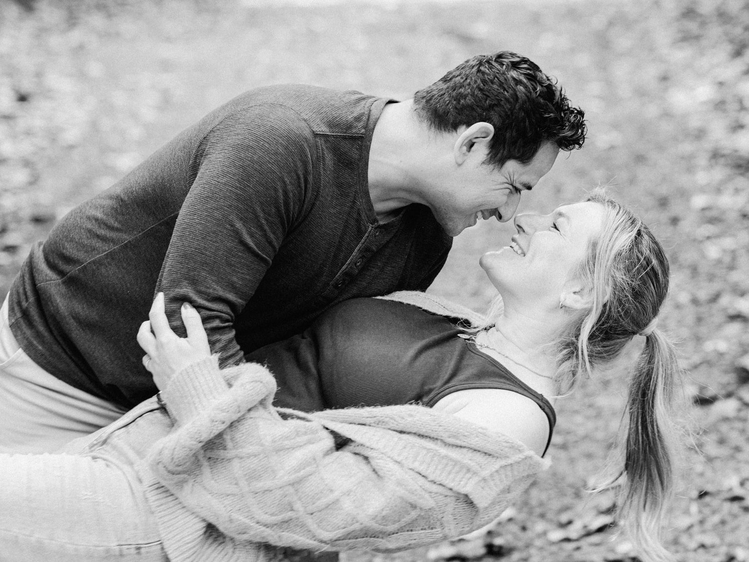 Black and white photo of a couple sharing a romantic moment, man leaning in to kiss smiling woman outdoors.