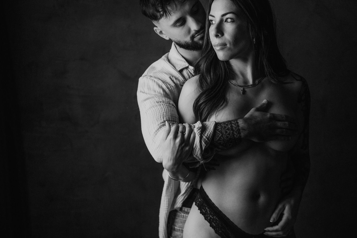 Black and white intimate couple portrait, man embracing woman from behind in a romantic studio photography session.
