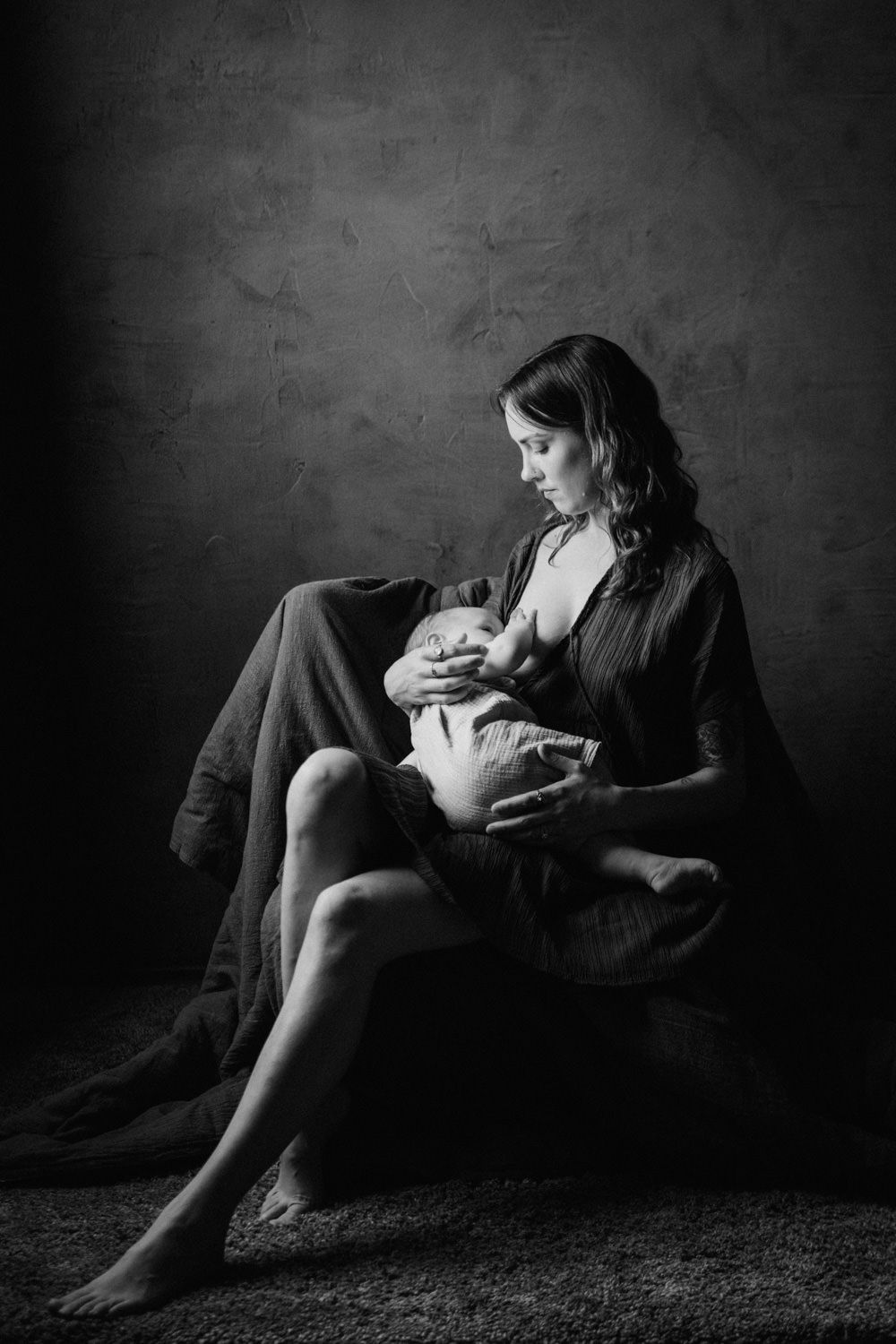 Black and white photo of a mother breastfeeding her newborn baby while seated in a chair.