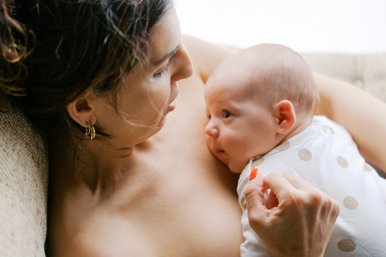 A mother gazes lovingly at her newborn baby while cradling them against her chest in a tender moment.