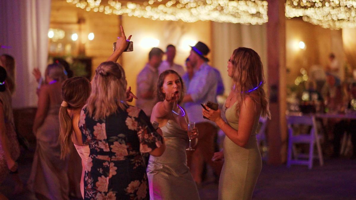 Guests dancing and celebrating at an elegant indoor wedding reception with warm string lights overhead.