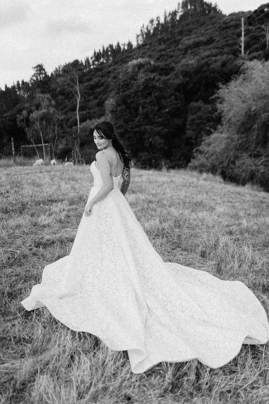 Bride in a stunning lace ball gown with long train poses in a field, black and white wedding photo.