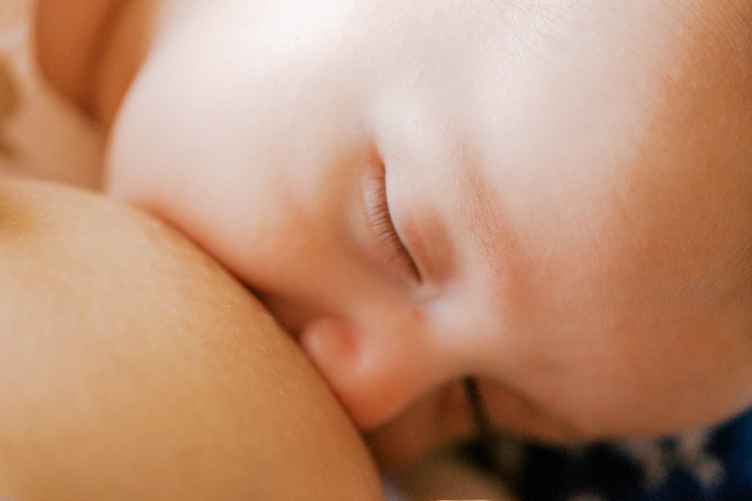 Close-up of a sleeping newborn baby breastfeeding, with soft skin and delicate eyelashes visible.