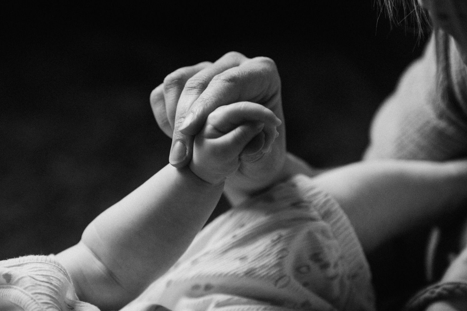 Black and white photo of a mother gently holding her newborn baby's tiny hand in a tender moment.
