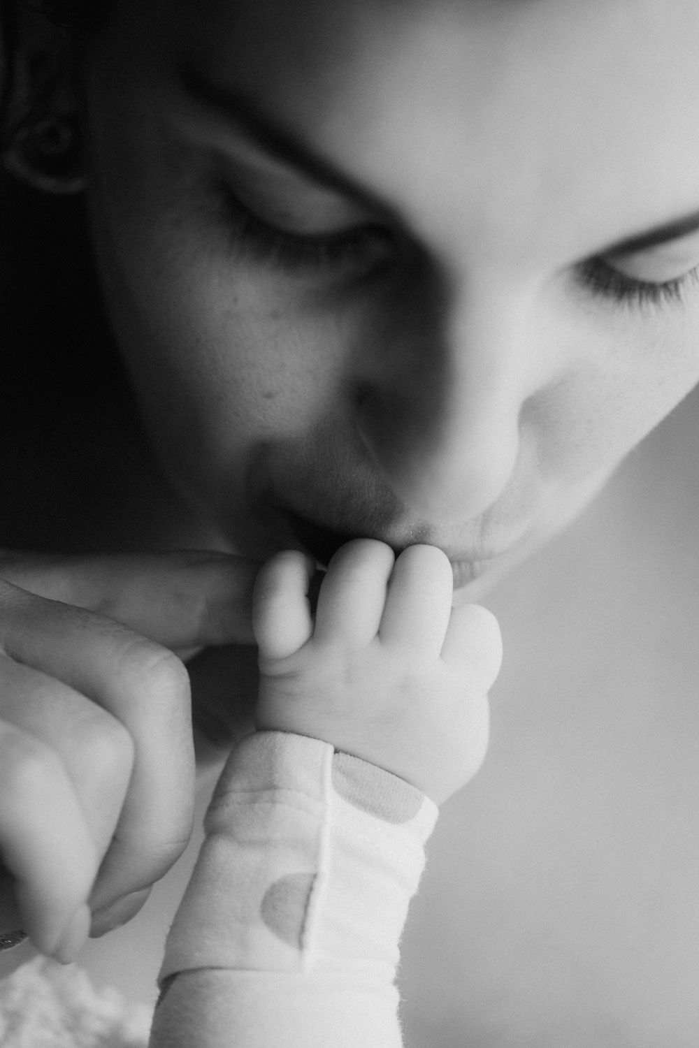 Black and white photo of a mother gently kissing her newborn baby's tiny hand in a tender moment.