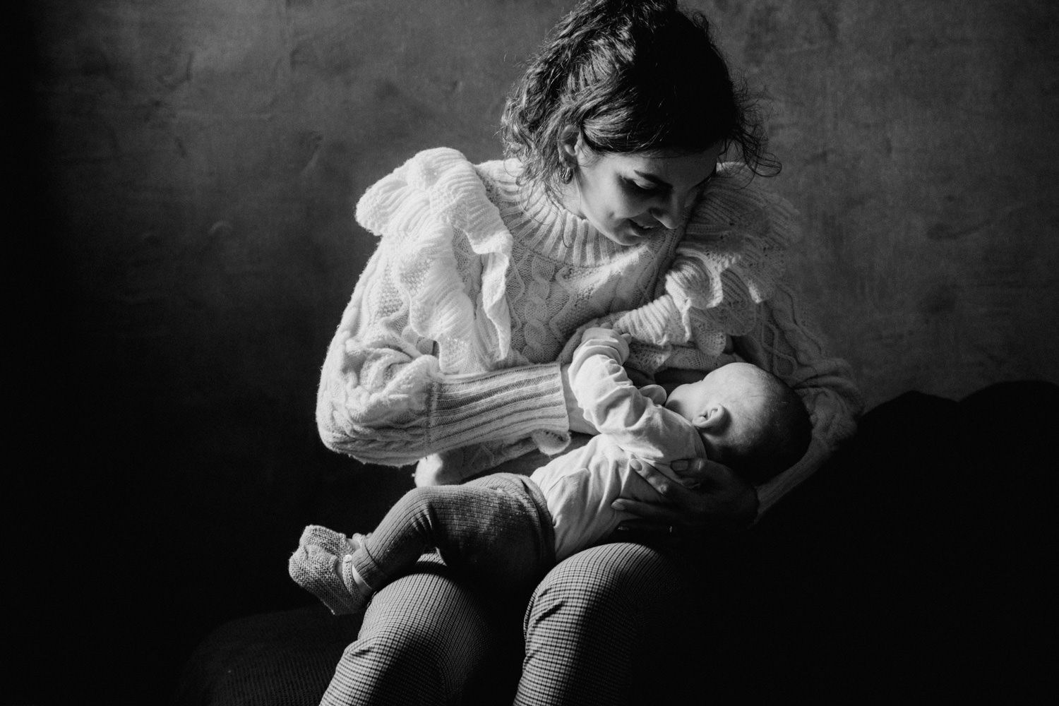 Black and white photo of a mother tenderly breastfeeding her newborn baby in soft natural light.