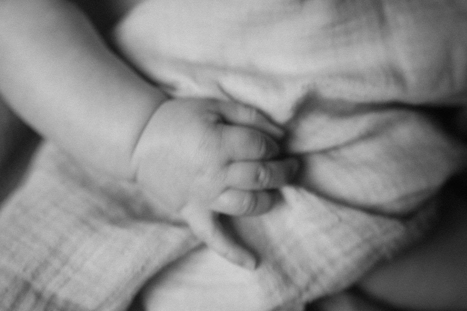 Close-up black and white photo of a newborn baby's tiny hand grasping a soft muslin blanket.