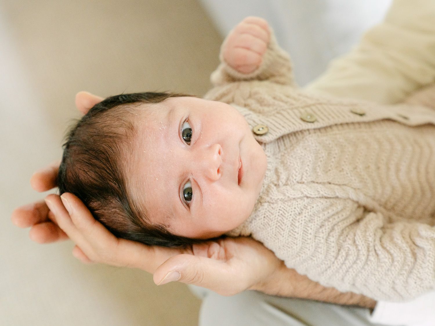 Close-up of a newborn baby in a knit sweater being gently cradled in parent's hands.