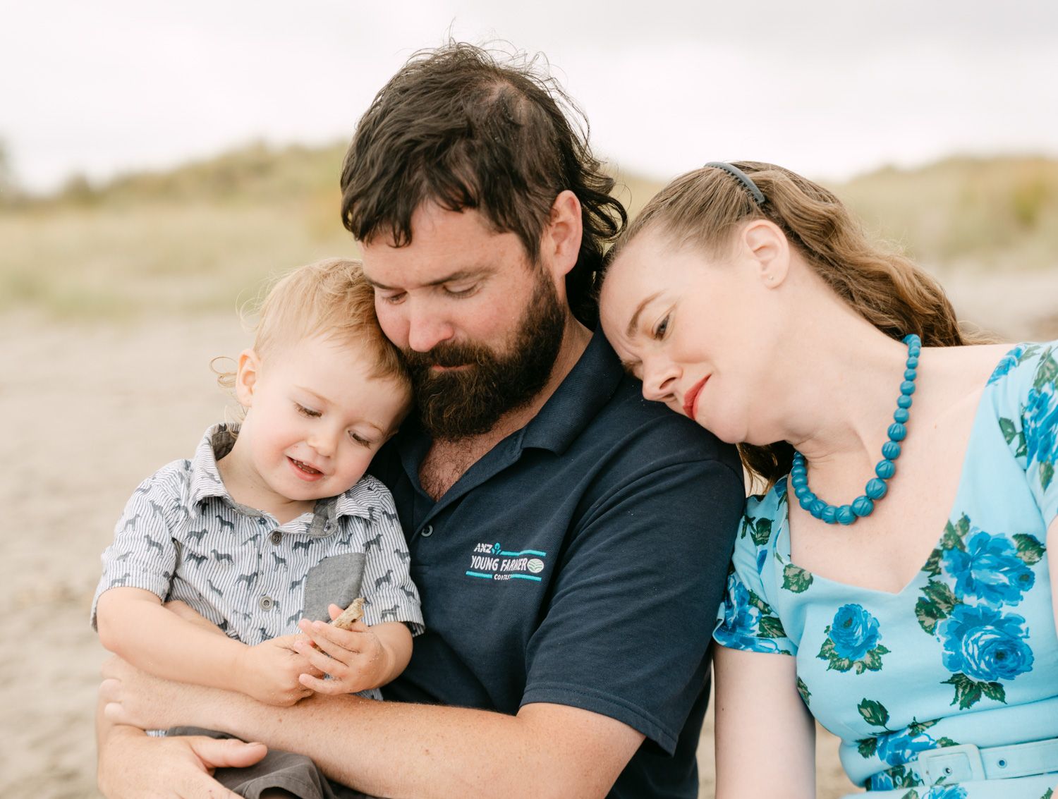 Family of three sharing a tender moment on a beach, father holding toddler son while mother leans in close.