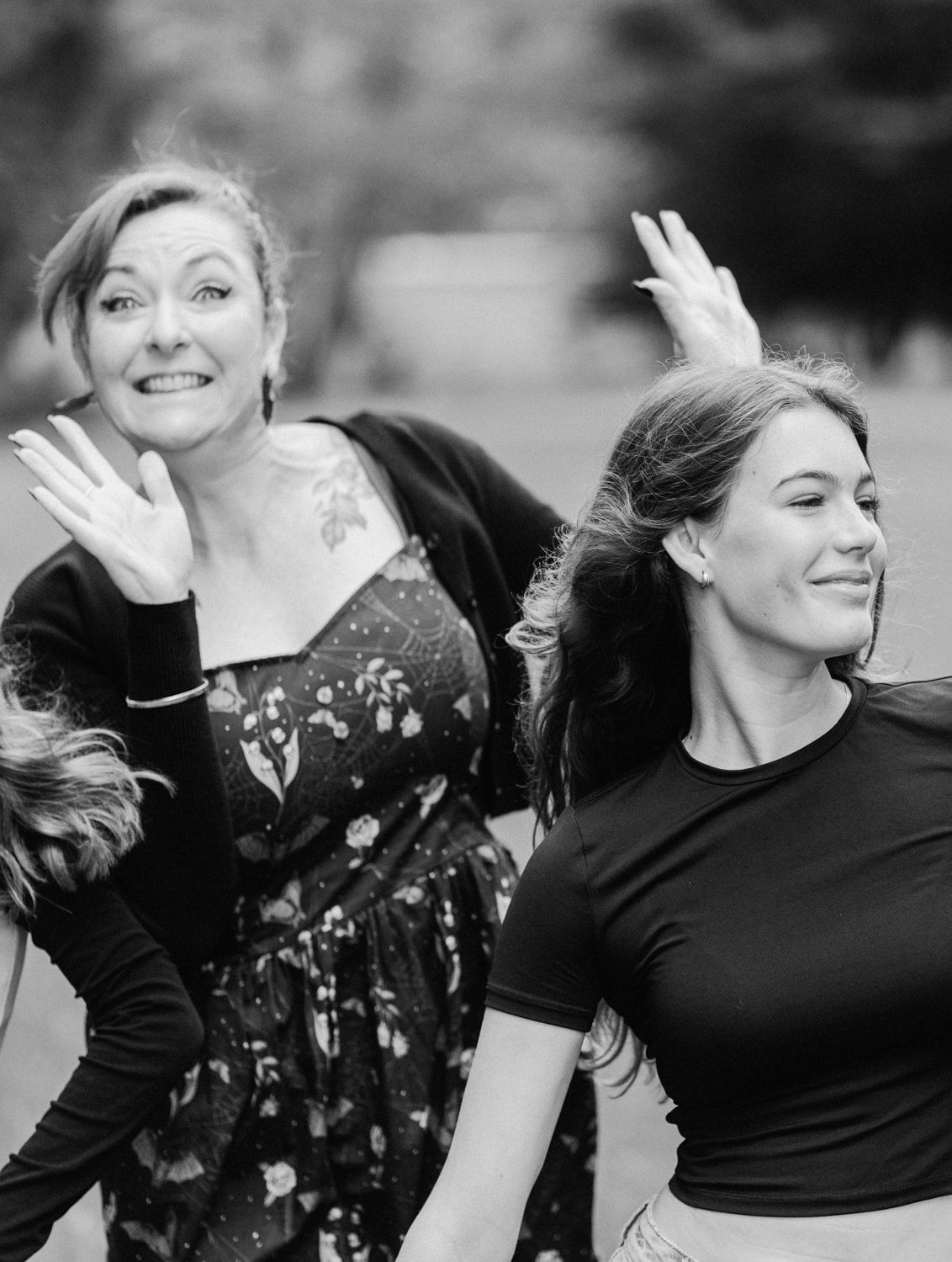 Two women laughing and posing outdoors in black and white photo, one in floral dress, one in black top.
